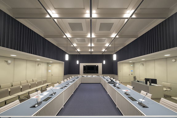 Op de afbeelding is commissiekamer 1 in het Eerste Kamergebouw te zien. De opstelling is een u-vormige tafel met stoelen eromheen.